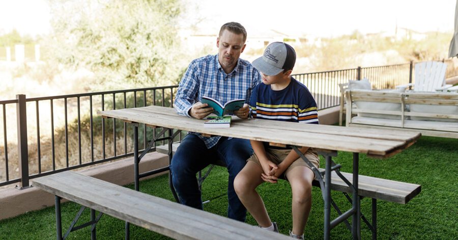 A homeschool father teaching his son while still together on a picnic bench.