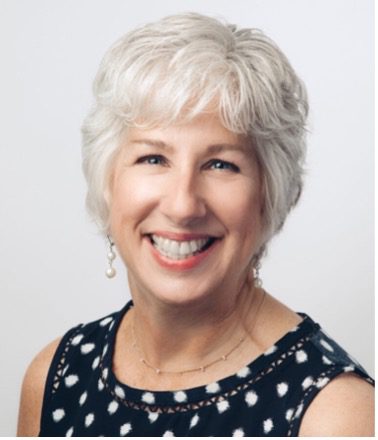 Lisa Bailey headshot. Woman with gray hair, a big smile, and a black and white polka dot shirt