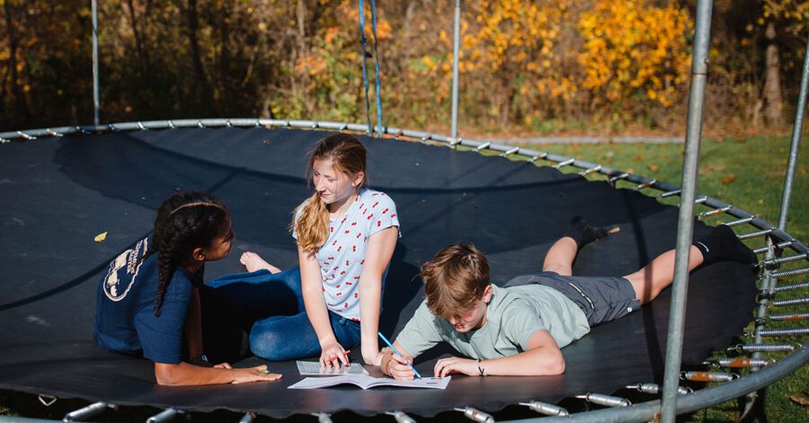Homeschool students studying for a blue book assessment on a tampoline