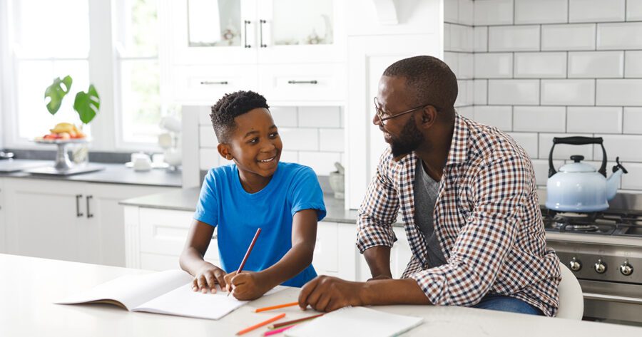 Happy African American father and son in kitchen. Planning a homeschool schedule and doing homework together. Family spending time at home. Father son relationship.