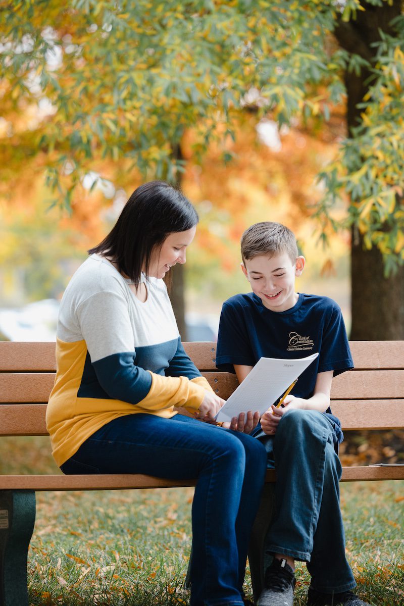 A homeschool mom teaching her son outside on a park bench