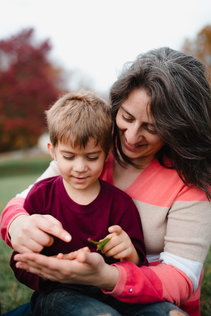 A mom holds her son outside, showing him something in her hand