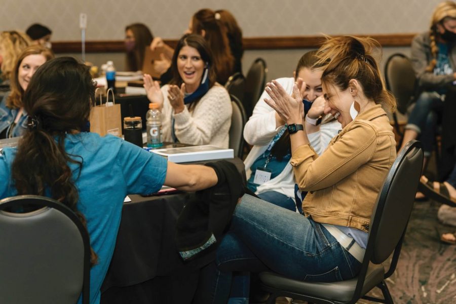 Sales Representatives clap and laugh around a table at the Las Vegas Sales Orientation