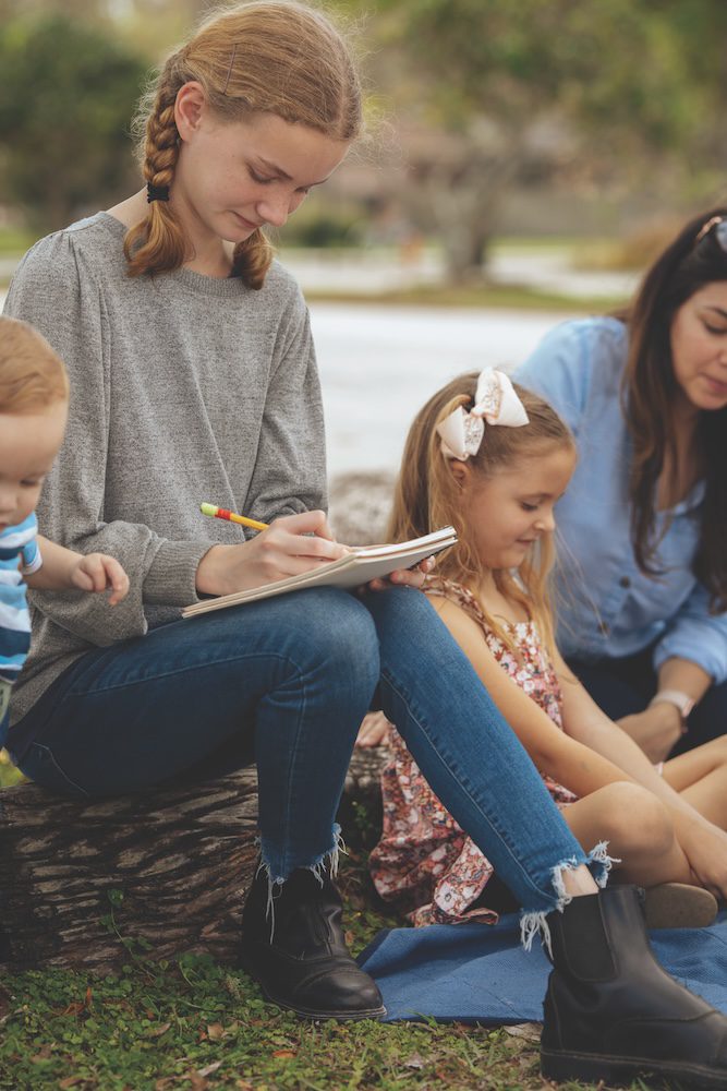 A family learns outside, an older student writing in a notebook