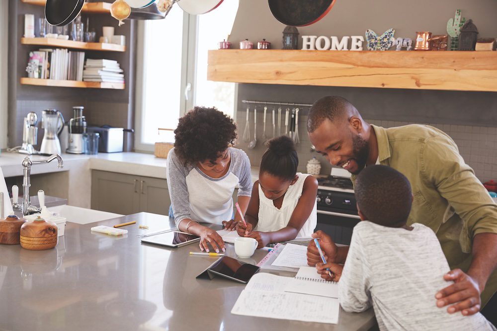 Parents Helping Children With Homework In Kitchen