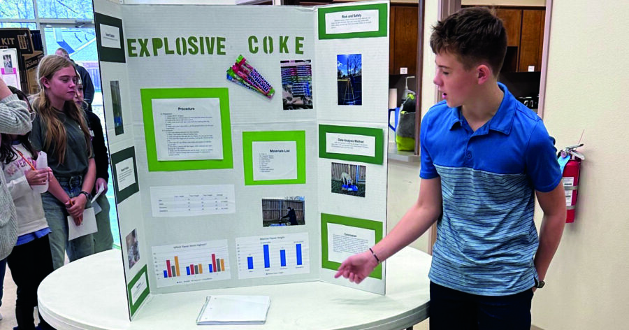 A homeschool boy presenting his science fair project on a trifold poster board.